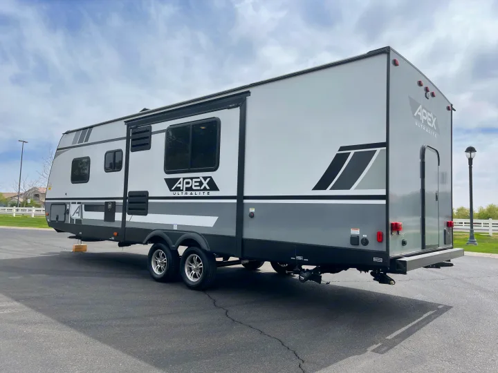 This Apex Ultralite travel trailer, a spacious RV rental option, is light gray and dark gray, parked outdoors.. Coachmen Apex 2021