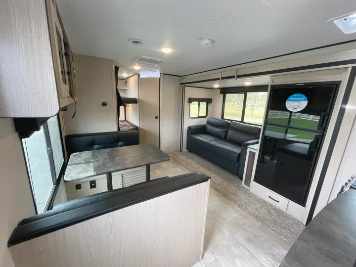 Inside a modern RV rental featuring a dinette, sleek sofa, refrigerator, and bunk beds for comfortable travel.. Coachmen Apex 2021