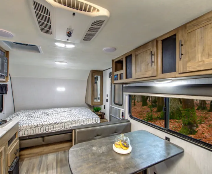 Cozy RV rental interior featuring a bed, dinette, kitchen, and a vibrant forest view from the large window.. Pioneer BH170 2021