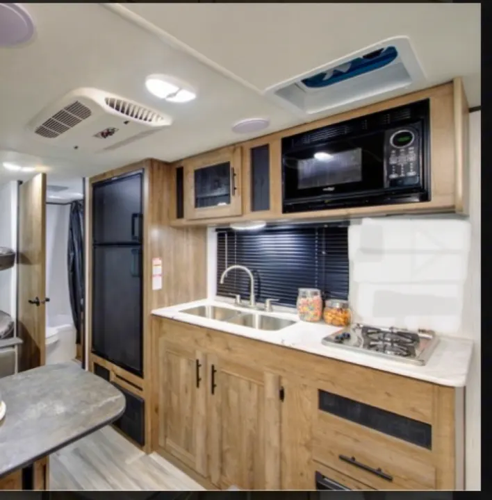 Modern RV rental kitchen features a double sink, gas stove, microwave, fridge, dining table, and access to a bathroom.. Pioneer BH170 2021