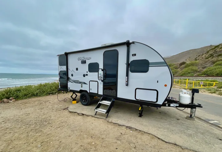 RV rental: A white Wolf Pup travel trailer parked on sandy ground by the ocean with distant hills under a cloudy sky.. Forest River Cherokee Wolf Pup 2021