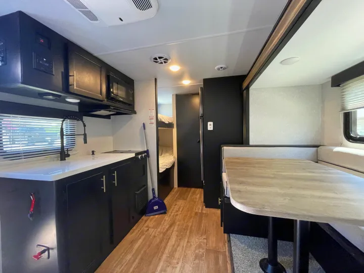 View inside a modern RV rental featuring a full kitchen, dining area, and a glimpse of cozy bunk beds.. Forest River Cherokee Wolf Pup 2021