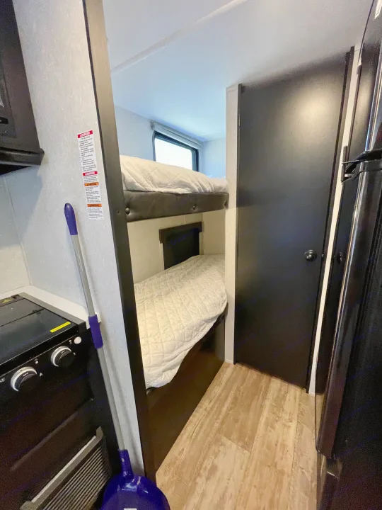 Cozy RV rental interior: bunk beds with white bedding, a stove, and a dark door. Perfect for family adventures.. Forest River Cherokee Wolf Pup 2021