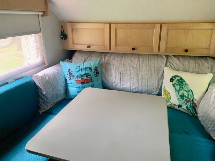 Inside a cozy RV rental: turquoise dinette cushions, overhead wood cabinets, and fun pillows create a comfy space.. T@B T16 2008