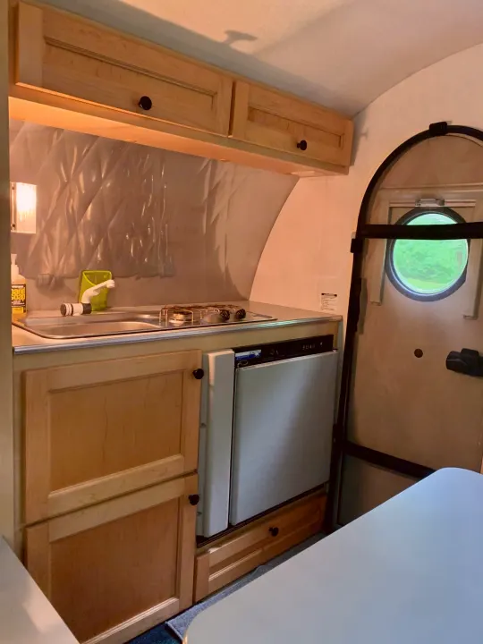 Inside a compact RV rental camper: a functional kitchen with sink, two-burner stove, small fridge, and wood cabinets.. T@B T16 2008