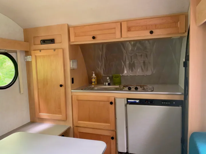 Compact RV rental interior with a functional kitchen featuring a sink, stovetop, refrigerator, light wood cabinets, and dining area.. T@B T16 2008