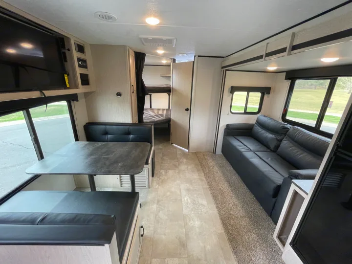 Inside an RV rental: well-lit living area with dinette, comfy sofa, TV, and rear bunk beds.. Coachmen Apex 2021