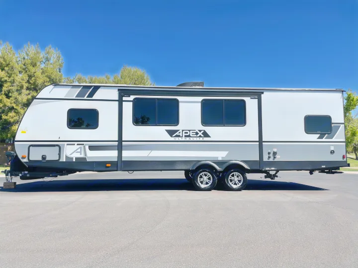 A sleek, modern Apex Ultralite travel trailer, ideal for an RV rental adventure. White & gray exterior on asphalt, sunny day.. Coachmen Apex 2021