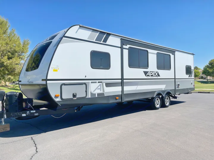 A sleek white and gray Apex travel trailer, an ideal rv rental for outdoor adventures, stands under a clear sky.. Coachmen Apex 2021