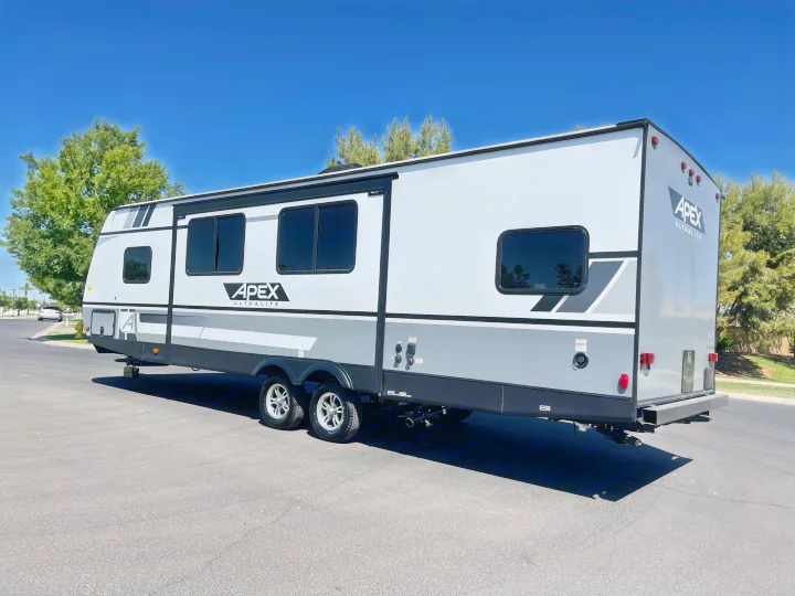 Modern grey and white Apex Ultralite rv rental, parked on asphalt under a clear blue sky, ready for travel.. Coachmen Apex 2021