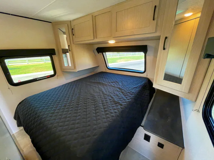 Relax in this RV rental bedroom with a comfy bed, dual windows overlooking nature, and ample storage.. Coachmen Apex 2021
