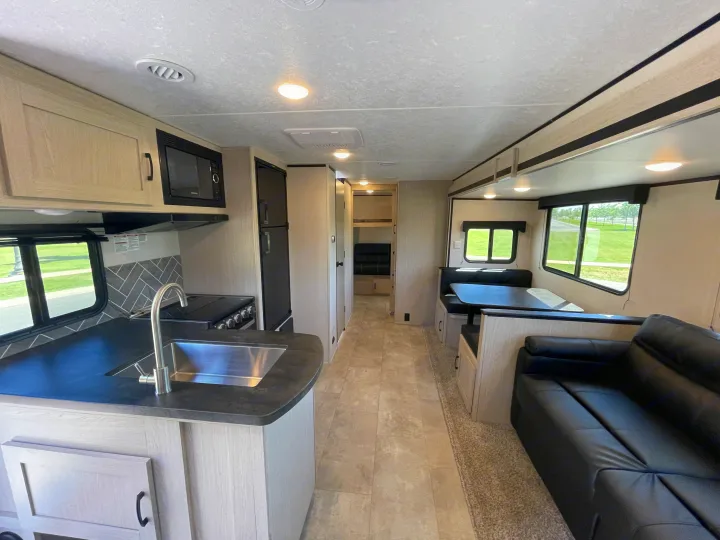 Spacious RV rental interior featuring a modern kitchen with stainless sink, dining booth, sofa, and bunk room access.. Coachmen Apex 2021