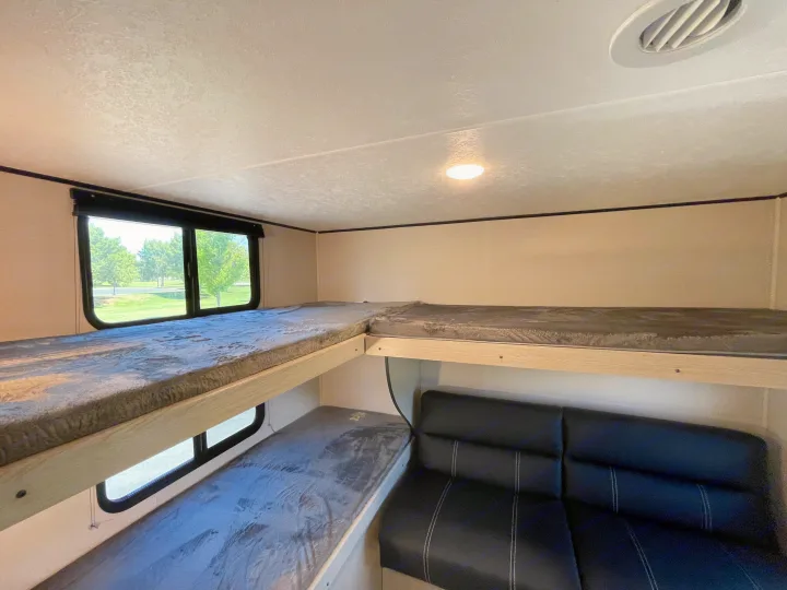 This RV rental interior features multiple bunk beds, a sofa, and windows with scenic views, ideal for travel.. Coachmen Apex 2021
