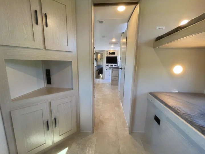 Explore this clean RV rental interior featuring a bright hallway, light wood cabinetry, and comfortable bunk beds with wall lighting.. Coachmen Apex 2021