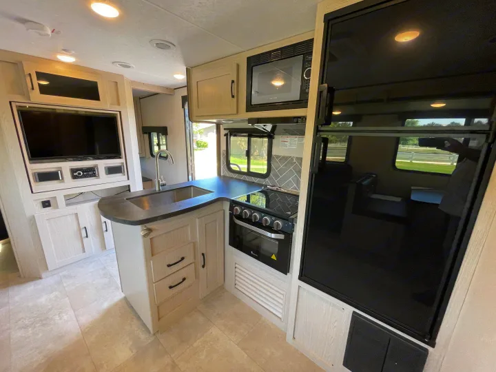 This RV rental showcases a modern interior: kitchen with stove, sink, fridge, microwave, plus an entertainment center with TV.. Coachmen Apex 2021