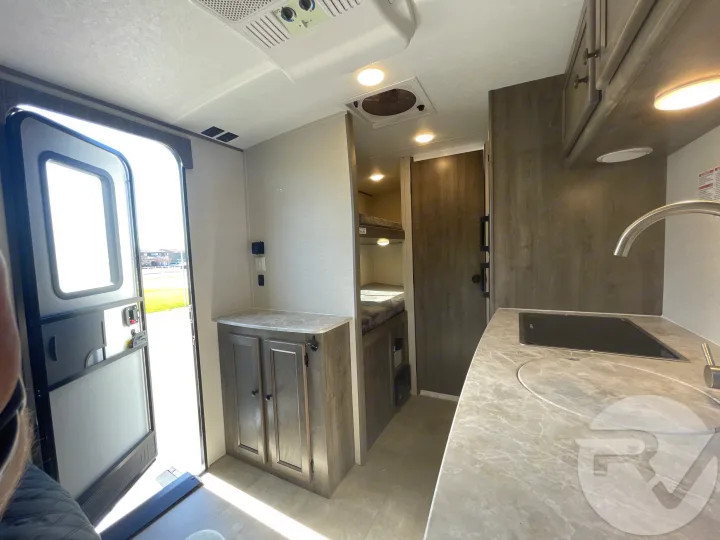 Step inside this RV rental, showcasing an open door, compact kitchen with sink/stovetop, and a cozy bunk bed area.. Coachmen Apex 2021