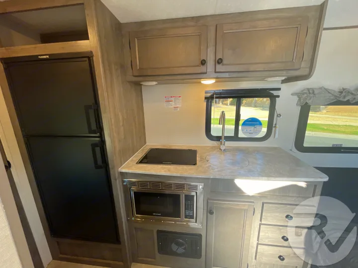 Well-equipped RV rental kitchen: Dometic fridge, built-in cooktop, sink, microwave, and ample cabinetry.. Coachmen Apex 2021