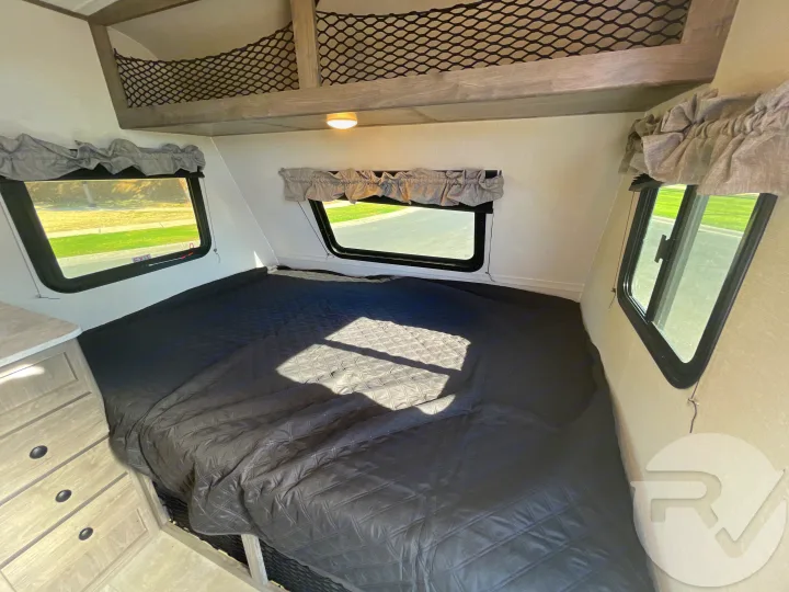 RV rental interior: cozy bedroom with a large quilted bed, multiple windows, and practical overhead netted storage.. Coachmen Apex 2021