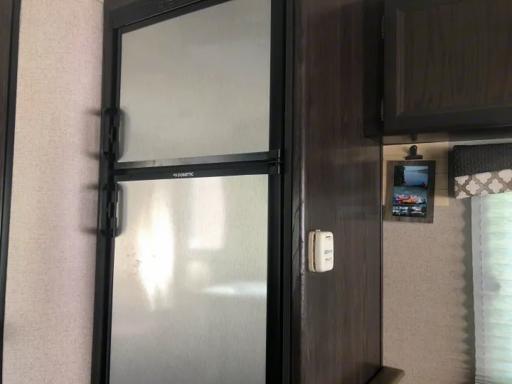 An RV rental interior featuring a Dometic refrigerator, dark wood cabinets, and light textured walls.. Dutchmen Kodiak 2019