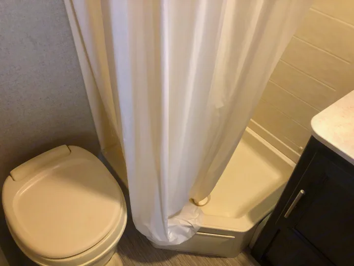 Compact RV rental bathroom featuring a toilet, shower with curtain, and vanity. Practical and functional for travelers.. Dutchmen Kodiak 2019