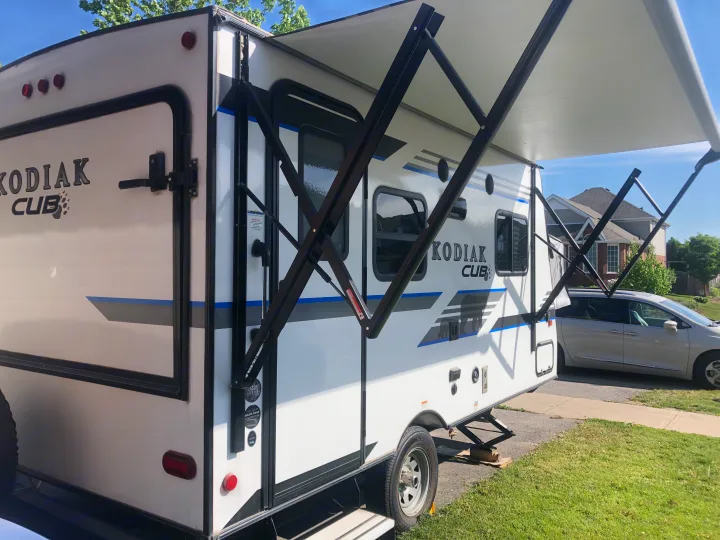 White Kodiak Cub travel trailer with extended awning, shown as an RV rental option parked on a driveway.. Dutchmen Kodiak 2019