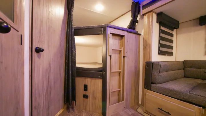 RV rental interior: Cozy bunk beds with ladder and comfortable sofa seating, ideal for family trips.. Forest River Alpha Wolf 26DBH-L 2021