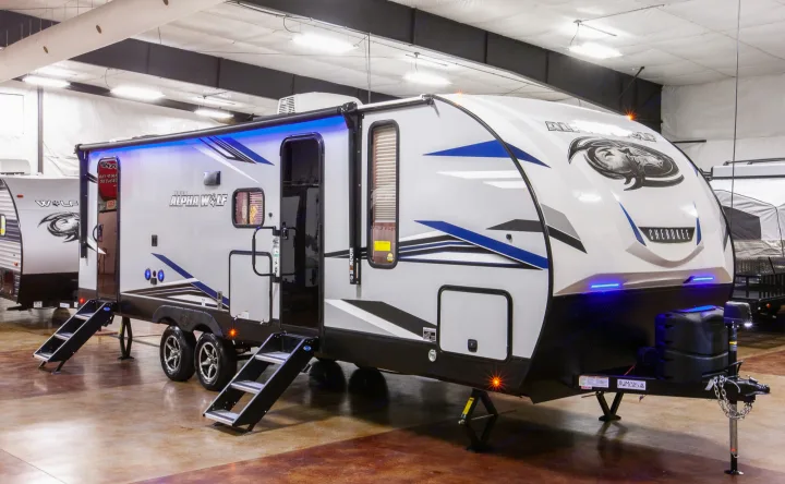 Cherokee Alpha Wolf travel trailer RV rental, with bright blue accent lights & extended steps inside a showroom.. Forest River Alpha Wolf 26DBH-L 2021