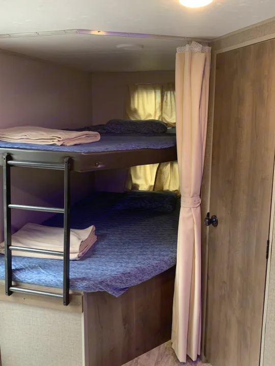 Cozy bunk beds in an RV rental, with blue bedding, privacy curtain, and windows. Great for family trips.. K-Z Manufacturing Connect 2018