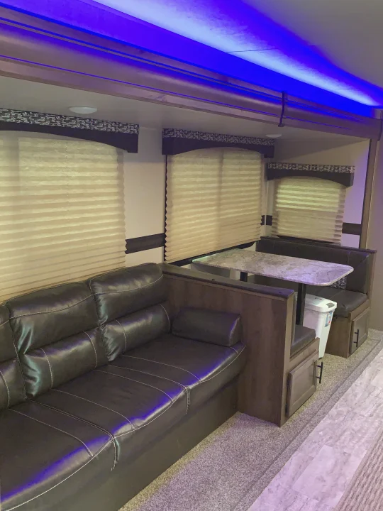 Explore this RV rental's cozy living and dining area, featuring a dark sofa, booth seating, and ambient blue LED lighting.. K-Z Manufacturing Connect 2018