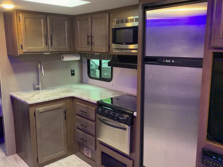 Interior of an RV rental kitchen showing light wood cabinets, microwave, stove, fridge, and sink. Ready for your travels.. K-Z Manufacturing Connect 2018