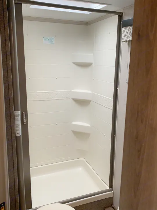 Bright, clean white shower with shelves and skylight inside a compact RV rental bathroom.. K-Z Manufacturing Connect 2018