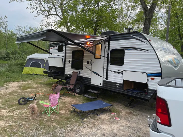 RV rental camping trip: A travel trailer with extended awning, tent, & dogs relaxing at a scenic outdoor campsite.. Forest River Puma 2019
