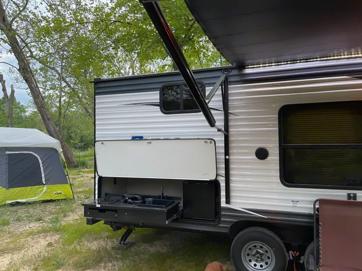 Perfect RV rental setup: a travel trailer with an open outdoor kitchen, awning lights, and a tent at a serene campsite.. Forest River Puma 2019