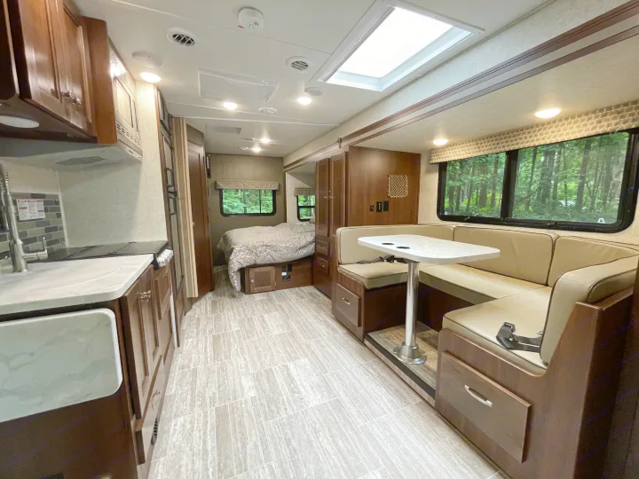Spacious RV rental interior featuring a full kitchen, dining booth, and cozy bedroom with wooded views.. Forest River Sunseeker 2019