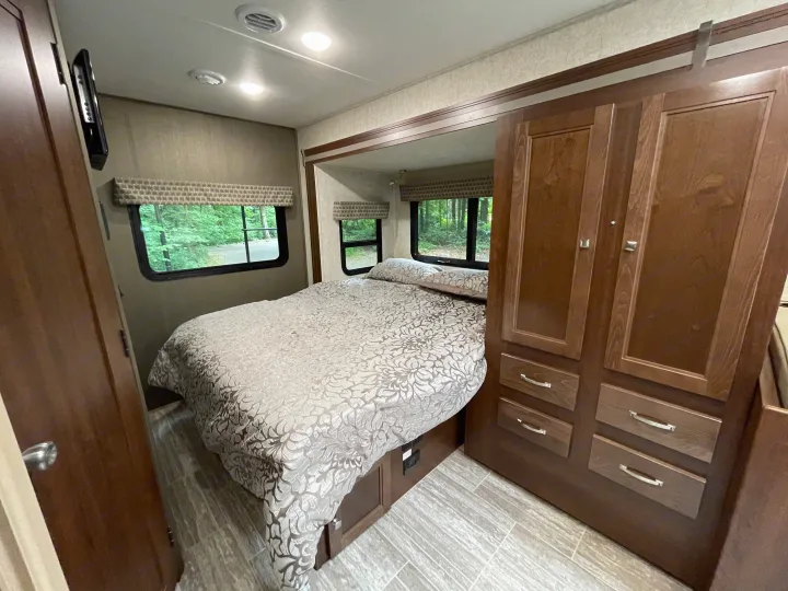 Inviting RV rental bedroom with patterned bed, wood cabinets, wall-mounted TV, windows, and wood-look flooring.. Forest River Sunseeker 2019