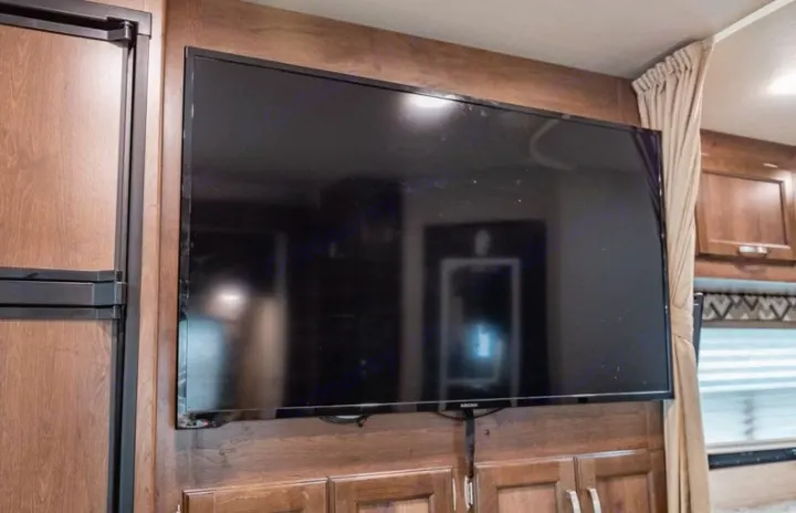 RV rental interior features a large, wall-mounted flat-screen TV for entertainment, alongside a refrigerator and cabinets.. Jayco Redhawk 2018