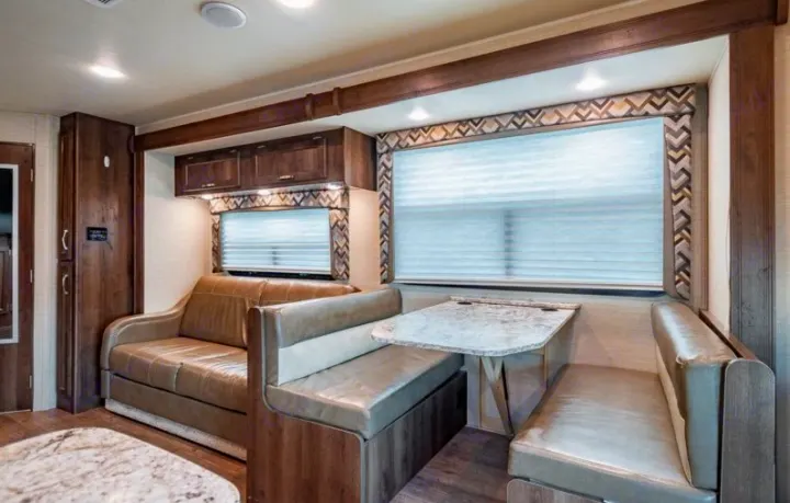 Spacious RV rental interior featuring a light-colored sofa, dinette with table & benches, wood cabinetry, & bright lighting.. Jayco Redhawk 2018