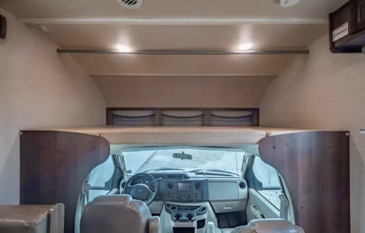 Interior of an rv rental: over-cab bunk bed with storage nets positioned above the driver's cockpit and dashboard.. Jayco Redhawk 2018