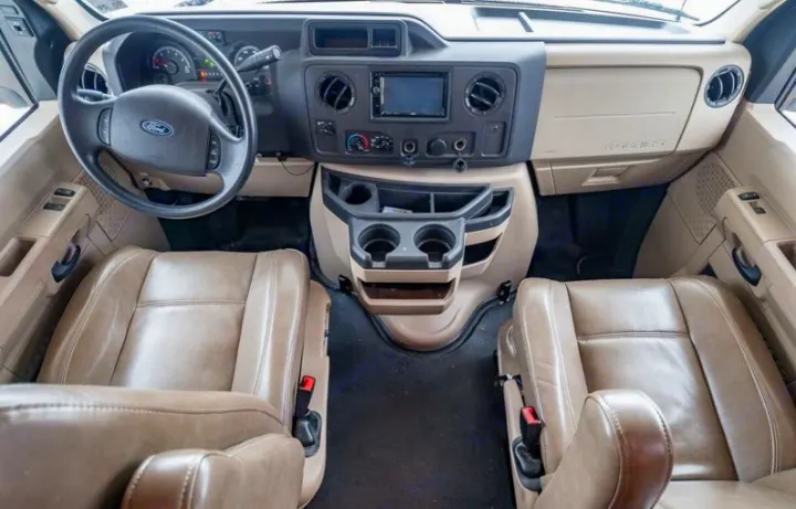 Spacious RV rental cockpit featuring comfortable tan captain's chairs, a Ford steering wheel, and a functional dashboard with cup holders.. Jayco Redhawk 2018