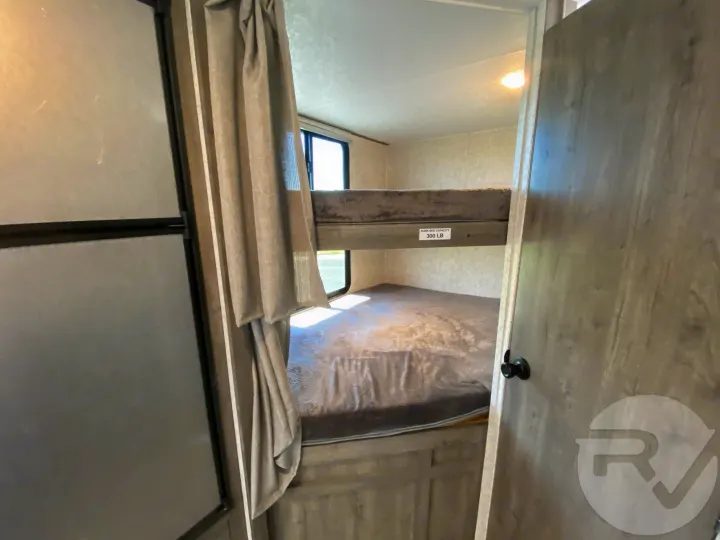 RV rental bunk beds (300 lb capacity) in a well-lit camper interior with window and privacy curtain.. Coachmen Apex 2021