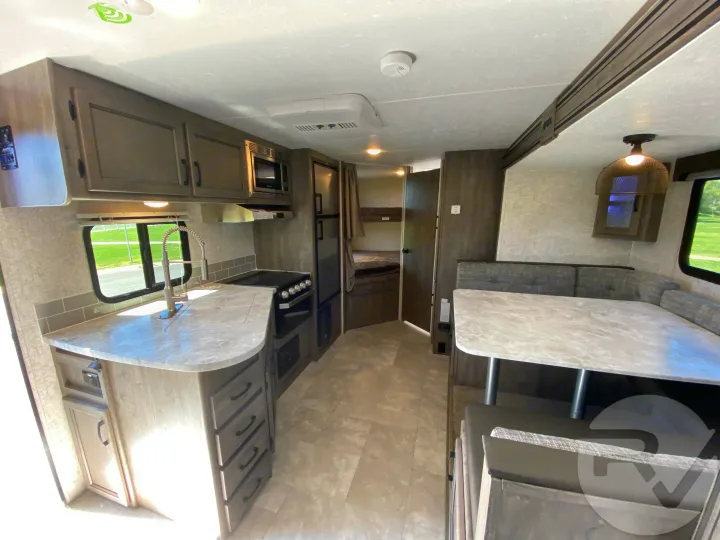 Bright RV rental interior featuring a full kitchen with sink, stove, & fridge, plus a dinette & bunk beds for comfortable travel.. Coachmen Apex 2021