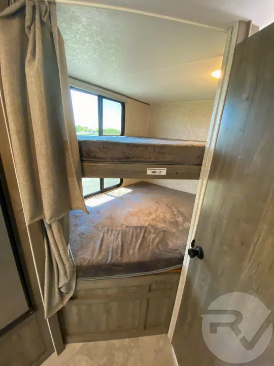 RV rental: Interior of a camper's bunk bed area, showing two beds, the top one rated for 300 lbs. Curtains & window on left.. Coachmen Apex 2021