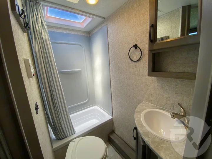 Compact RV rental bathroom featuring a shower/tub combo with a skylight, toilet, sink, vanity, and mirror.. Coachmen Apex 2021