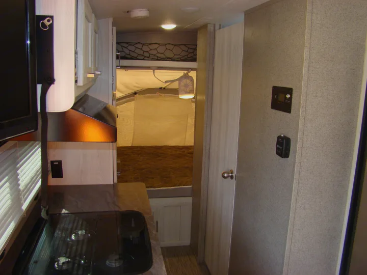 Inside an RV rental showing kitchen area with stove, cabinets, and TV, plus an expandable tent bed with a fan. Great for travel!. Forest River Rockwood 2019