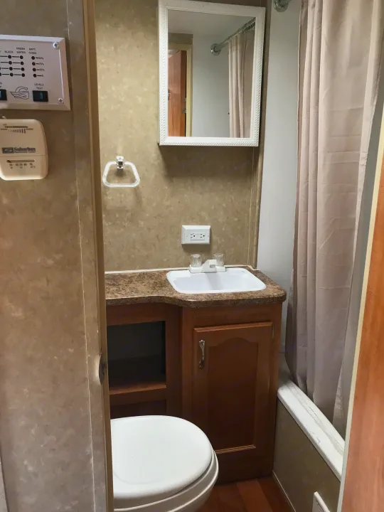 RV rental bathroom interior: a compact space with sink, toilet, shower curtain, tank monitor, and thermostat.. Gulf Stream Ameri-Lite 25 BS 2008