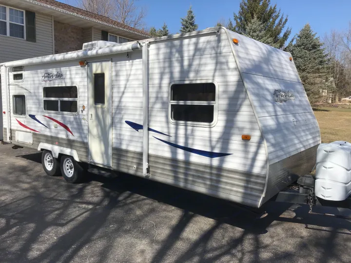 Bright white travel trailer RV with red/blue stripes & awning, parked on a paved driveway. Ideal for an rv rental.. Gulf Stream Ameri-Lite 25 BS 2008