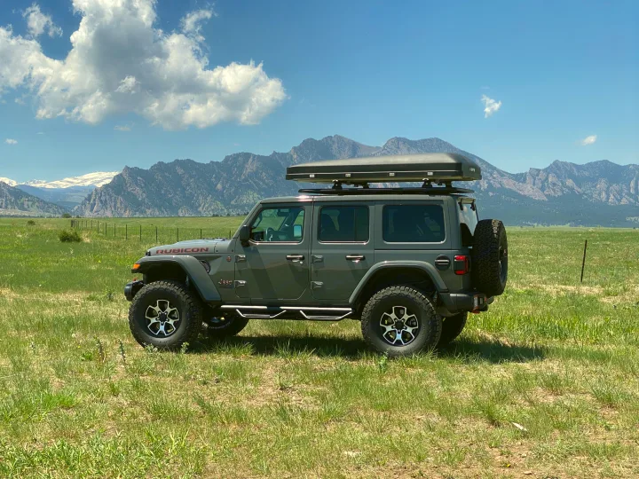 Experience RV rental freedom! A gray Jeep Wrangler with a rooftop tent sits in a scenic mountain field.. Jeep Wrangler Unlimited 2021