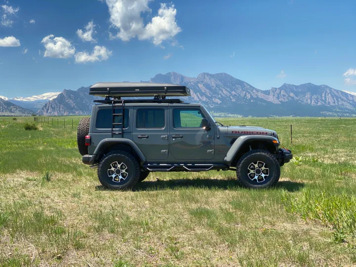 Explore nature: Gray Jeep Wrangler Rubicon with rooftop tent in a scenic mountain field, available for rv rental.. Jeep Wrangler Unlimited 2021