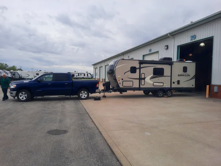 Blue pickup truck and tan Mini Lite RV at an rv rental facility. The travel trailer is outside a garage, with a man walking nearby.. Forest River Rockwood Mini Lite 2021