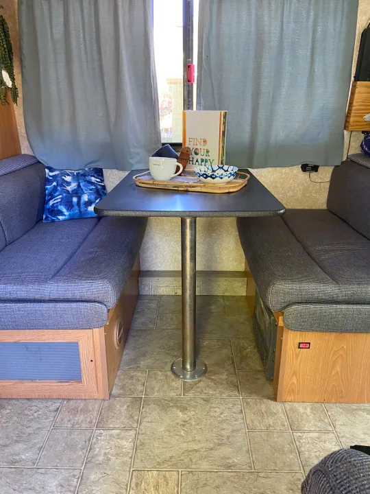 Cozy RV rental dinette featuring grey fabric bench seating, a center table with coffee, and an open book.. Thor Motor Coach Four Winds Majestic 2009